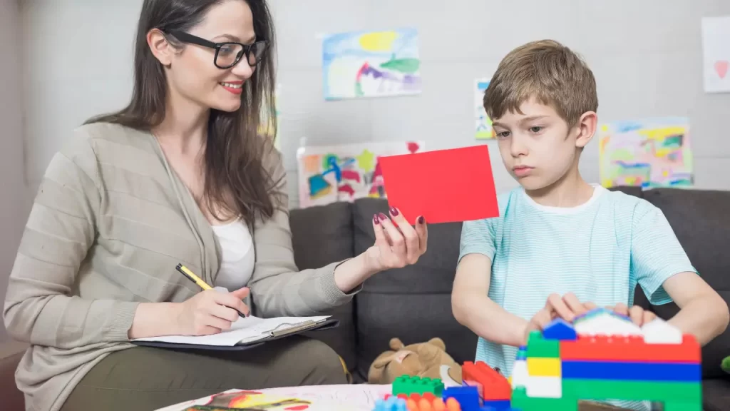 Psicóloga infantil conversando com criança em sala colorida e segura.